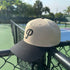 Beige and black cap with a 'P' logo on a tennis court fence